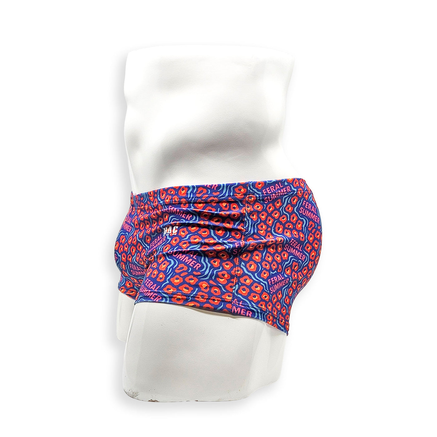 Side view of male model wearing HAC Swim Feral Summer Box Cut swim trunk with low-rise fit and bold blue, pink and orange graphic print.