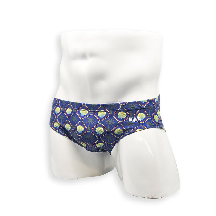 Men’s palm and shell print swim brief – Basic cut angled front view in deep blue with gold shells and palm tree pattern, contoured fit