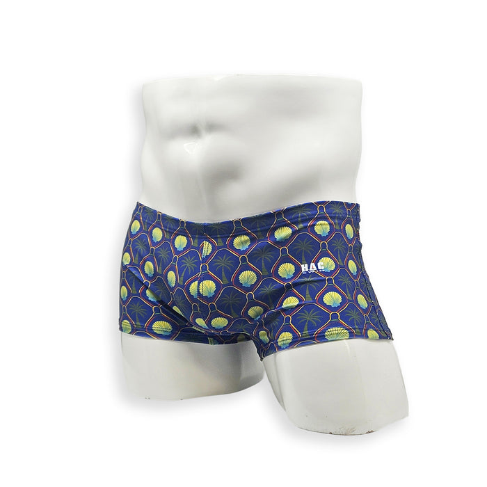 Men’s palm and shell print swim trunk – Box cut angled front view in deep blue with gold shell and palm pattern, low-rise fit